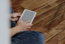 Close-up of hands holding an e-reader on a wooden floor, depicting a casual reading moment.