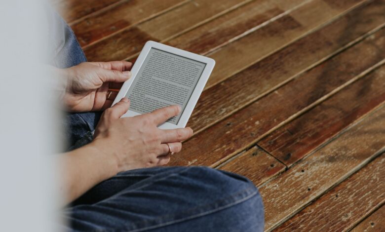 Close-up of hands holding an e-reader on a wooden floor, depicting a casual reading moment.