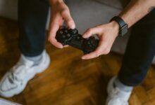A person holding a gaming controller indoors, wearing casual attire with a smartwatch.