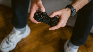 A person holding a gaming controller indoors, wearing casual attire with a smartwatch.