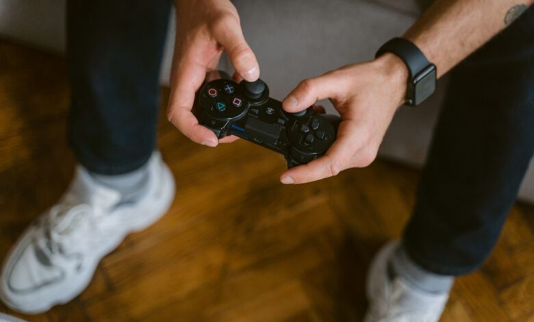 A person holding a gaming controller indoors, wearing casual attire with a smartwatch.