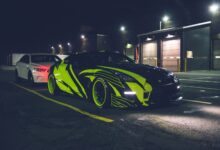 Contemporary black automobile with yellow wrapping decal design and headlights on parking lot in city street at night time outside