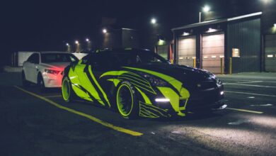 Contemporary black automobile with yellow wrapping decal design and headlights on parking lot in city street at night time outside
