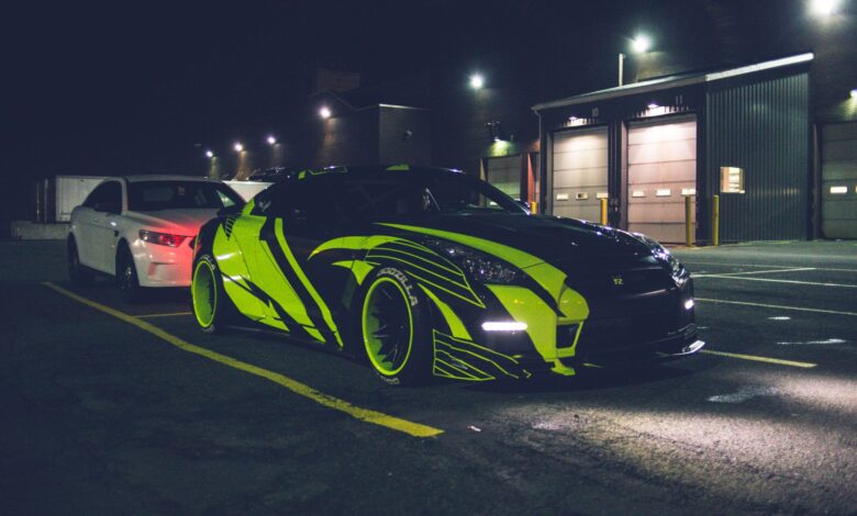 Contemporary black automobile with yellow wrapping decal design and headlights on parking lot in city street at night time outside
