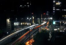 Night view of a bustling highway in Warsaw, Poland, featuring light trails and urban skyscrapers.