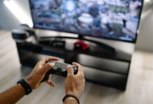 Close-up of hands holding a gaming controller while playing video games indoors.