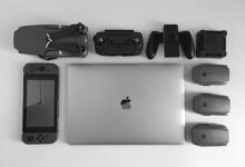 A black and white flat lay of various modern tech gadgets including a laptop, drone, and gaming device.