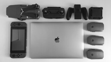 A black and white flat lay of various modern tech gadgets including a laptop, drone, and gaming device.