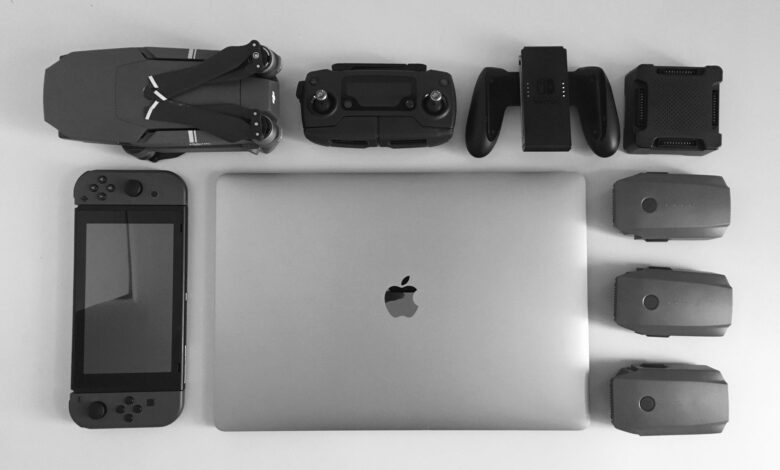 A black and white flat lay of various modern tech gadgets including a laptop, drone, and gaming device.