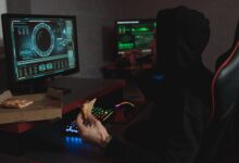 Hacker in a black hoodie eating pizza and drinking soda while analyzing data on multiple computer screens.