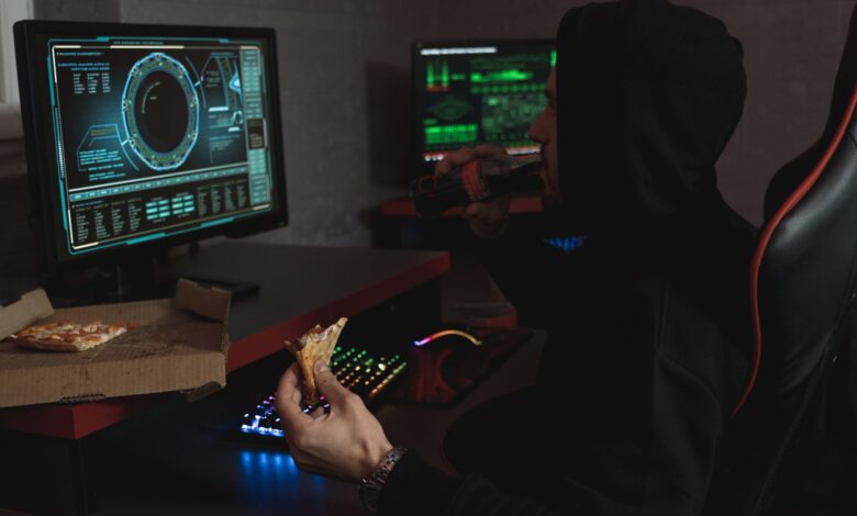 Hacker in a black hoodie eating pizza and drinking soda while analyzing data on multiple computer screens.