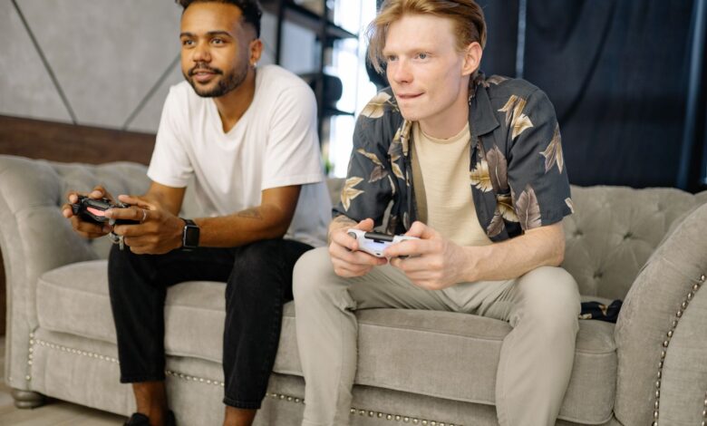 Two friends sitting on a sofa, playing video games together at home.