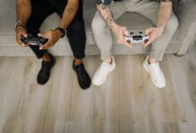 Two friends with gaming controllers focusing on a video game indoors from above.