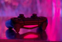 A wireless game controller in focus with a vibrant pink and purple neon background.