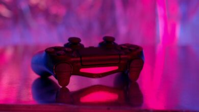 A wireless game controller in focus with a vibrant pink and purple neon background.