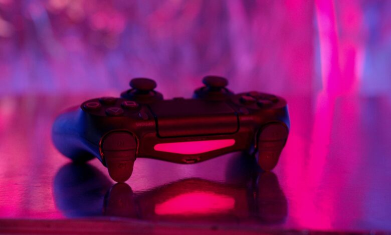 A wireless game controller in focus with a vibrant pink and purple neon background.