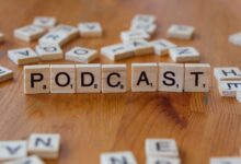 Scrabble tiles arranged to spell 'PODCAST' on a wooden surface with scattered letters.