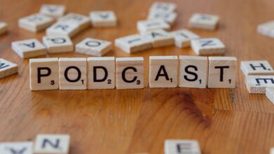 Scrabble tiles arranged to spell 'PODCAST' on a wooden surface with scattered letters.