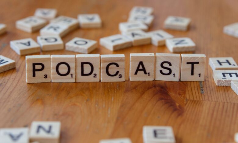 Scrabble tiles arranged to spell 'PODCAST' on a wooden surface with scattered letters.