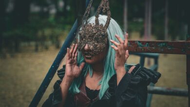 A woman with green hair wearing an ornate rabbit mask poses outdoors, exuding a mysterious vibe.