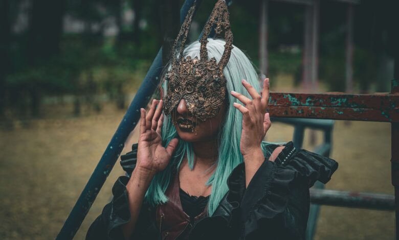 A woman with green hair wearing an ornate rabbit mask poses outdoors, exuding a mysterious vibe.