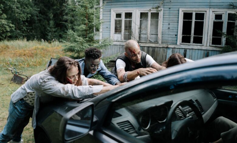 A group of zombies surround a car in front of an old, abandoned house.
