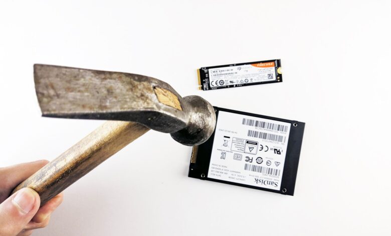 Close-up image of a hammer poised to strike a hard drive and SSD, symbolizing data destruction.