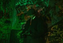 Stylish man in a trench coat and hat standing against vibrant graffiti wall, exuding retro elegance.