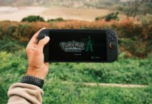 A person holds a handheld gaming device outdoors with Pokémon Legends on screen.