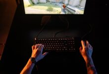 A gamer intensely playing a first-person shooter game on a computer setup indoors at night.