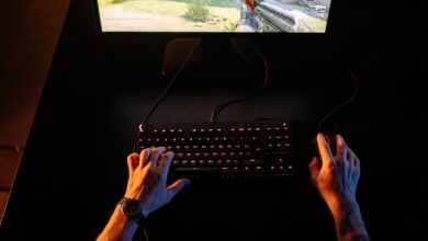 A gamer intensely playing a first-person shooter game on a computer setup indoors at night.