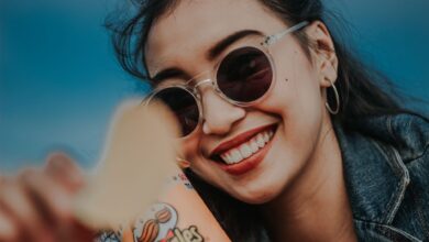 Smiling woman in sunglasses and denim jacket holding Pringles chip outdoors.