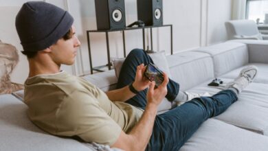 Casual young man playing mobile games on sofa with speakers in the background.