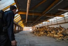 An urban explorer inspects the interior of an abandoned warehouse filled with debris.
