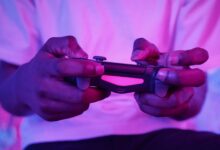 Close-up of an adult holding a video game controller with pink lighting, highlighting gaming experience.