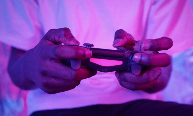 Close-up of an adult holding a video game controller with pink lighting, highlighting gaming experience.