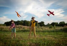Two kids enjoying a sunny day outdoors, playing with toy airplanes.