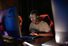 Young adult male intensely focused on computer gaming, using headset and gaming keyboard indoors.