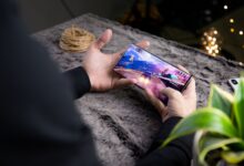 From above of crop anonymous person playing video game on modern cellphone with image of car on screen