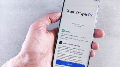 Close-up of a hand holding a Xiaomi smartphone with HyperOS interface, showcasing comprehensive refactoring and system update details.