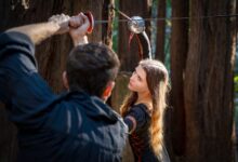 A man and woman engage in a historical sword duel in the woods.