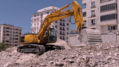 Yellow excavator working on urban construction site amidst rubble and buildings in Kahramanmaraş, Türkiye.