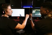 Two male friends fist bump at a computer gaming station, showcasing teamwork and camaraderie.