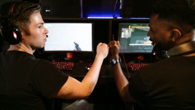 Two male friends fist bump at a computer gaming station, showcasing teamwork and camaraderie.