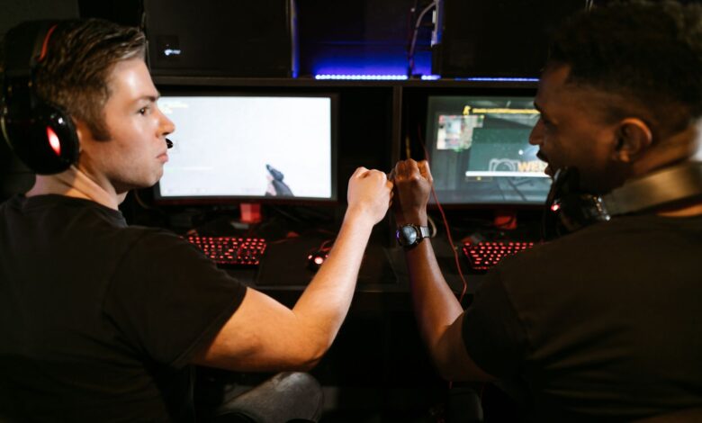 Two male friends fist bump at a computer gaming station, showcasing teamwork and camaraderie.