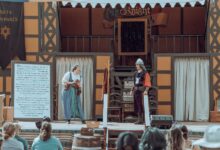 Actors in medieval costumes performing on an outdoor stage before an audience.
