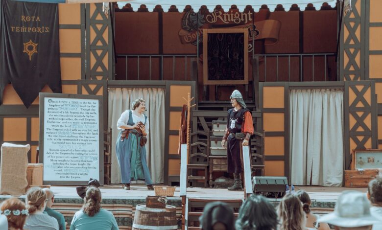 Actors in medieval costumes performing on an outdoor stage before an audience.