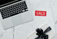 Top-down view of a laptop and gift with a sale sign on marble background.