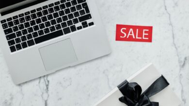 Top-down view of a laptop and gift with a sale sign on marble background.