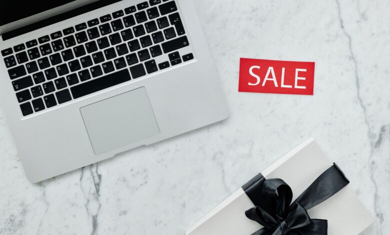 Top-down view of a laptop and gift with a sale sign on marble background.